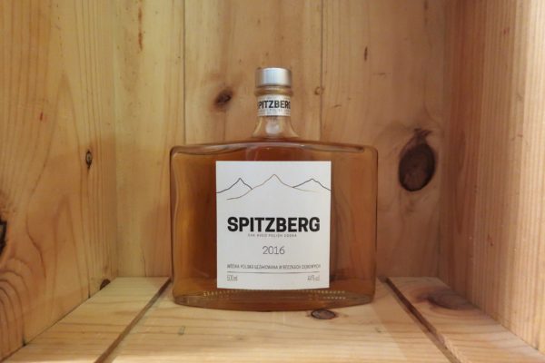 Eine transparente Glasflasche mit silbernen Verschluss und weiß-grauem Etikett steht in einer Holzkiste.