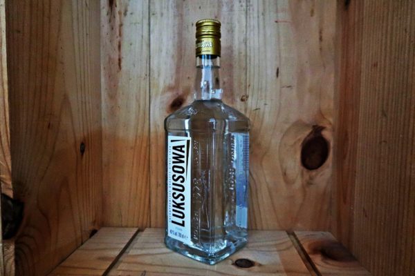Eine transparente Glasflasche mit weißem Etikett, steht in einem Holzkasten.
